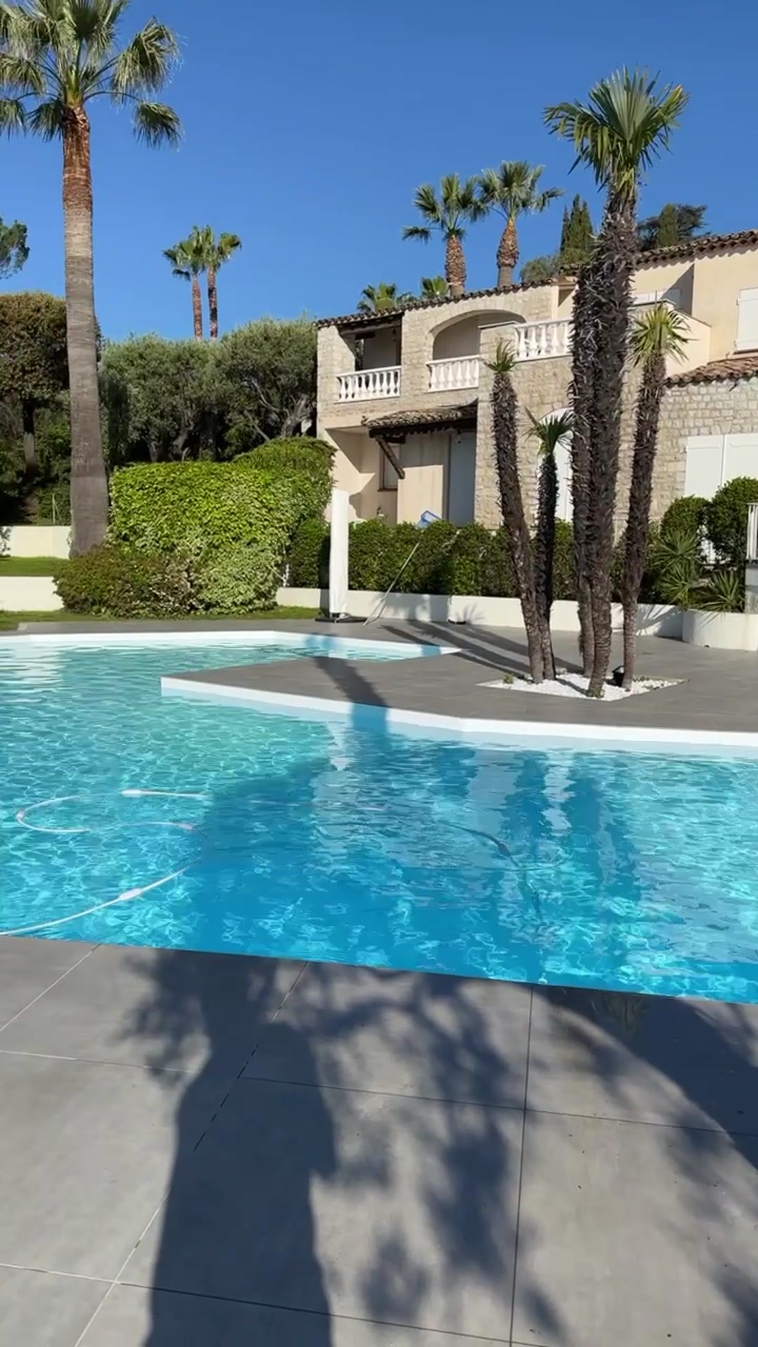 Piscine blanche bordée de palmiers devant une villa en pierre