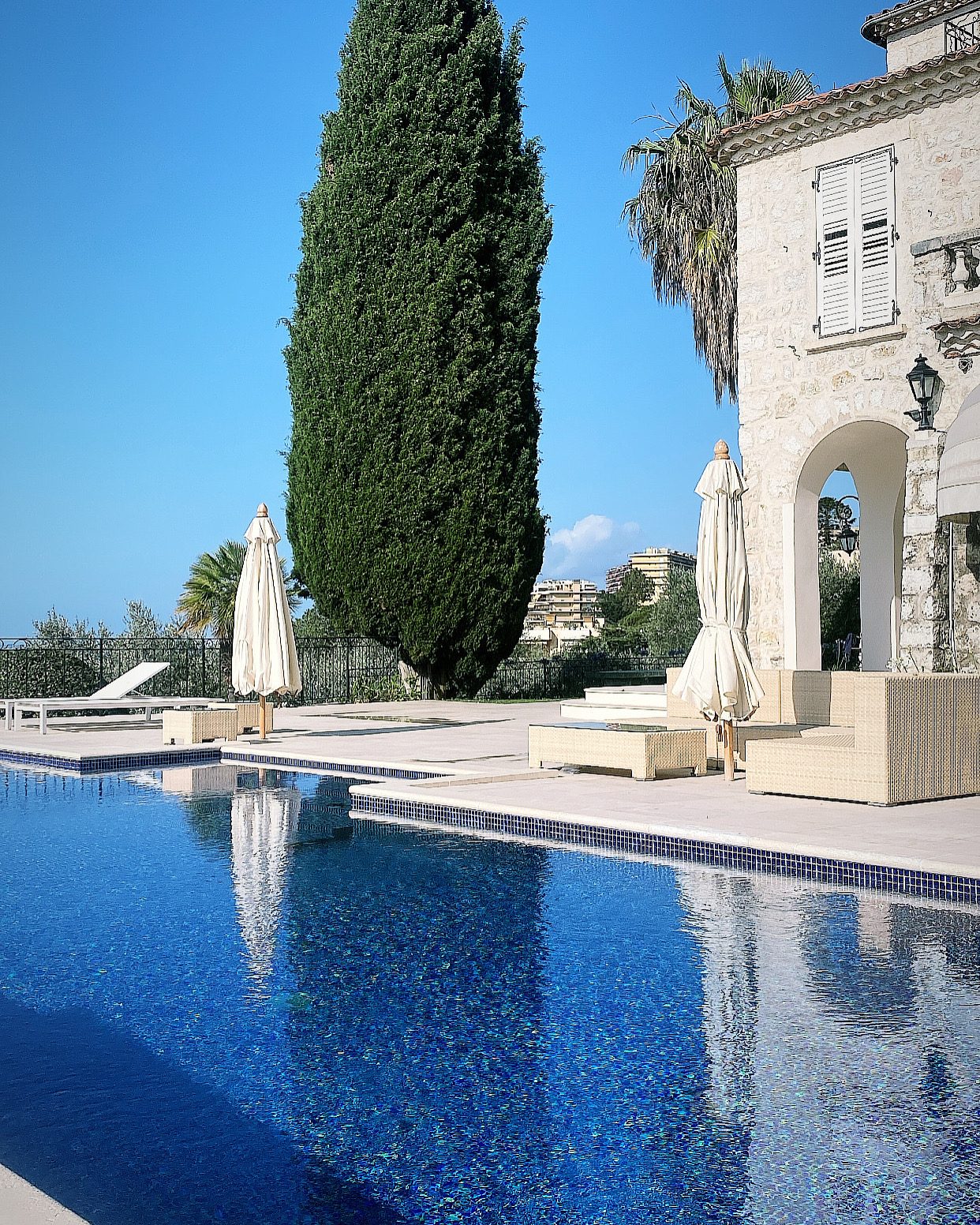 Piscine en mosaïque bleue devant une bastide en pierre et un cyprès